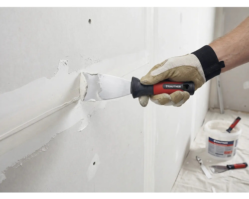 Hantverkare spacklar väggen med spackel och spackel. Rautner Logo syns.