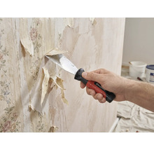 En person tar bort gammal tapet från en vägg med en spackelspade.