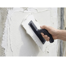 En person applicerar puts på en vägg med en murslev.