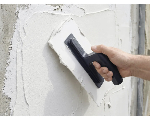 En person applicerar puts på en vägg med en murslev.