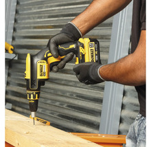 En hantverkare använder en gul sladdlös gipsskruvdragare från DeWalt för att skruva in en skruv i en träplanka.