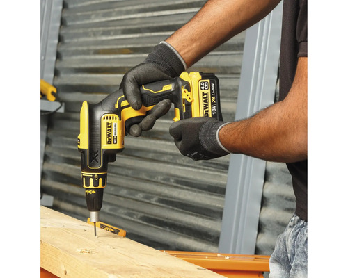 En hantverkare använder en gul sladdlös gipsskruvdragare från DeWalt för att skruva in en skruv i en träplanka.