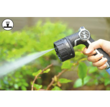 Hand håller trädgårdsslangsprutpistol medan du vattnar växter