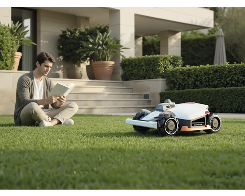 Man läser bok i trädgården bredvid robotgräsklipparen.