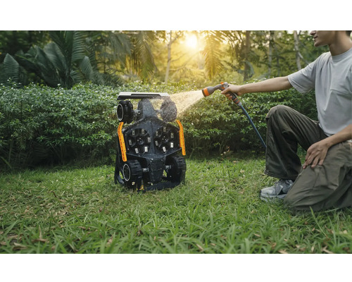Man rengör en robotgräsklippare med en vattenslang i trädgården.