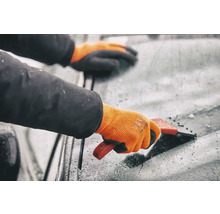 Person med handskar använder en isskrapa på en vindruta