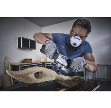 Användare med andningsskydd, skyddsglasögon och handskar bearbetar trä med en vinkelslip