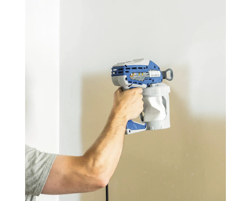 En person håller en färgsprutpistol framför en vägg