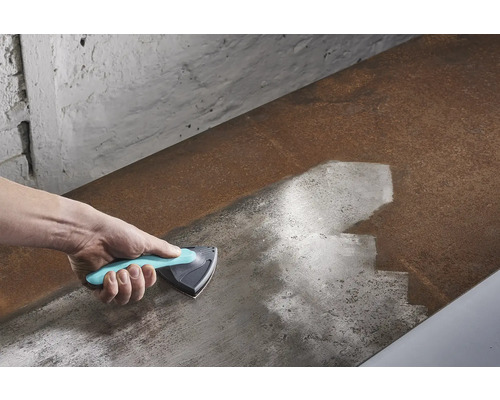 Hand med trekantsskrapa som rengör en metallyta