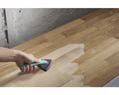 En person applicerar ytbehandling med en trekantig borste på en träskiva.