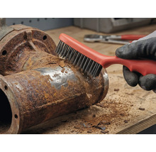 En person tar bort rost från ett metallrör med en stålborste.