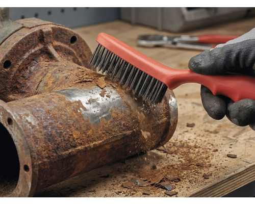 En person tar bort rost från ett metallrör med en stålborste.