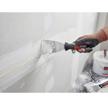 En person spacklar en vägg med spackel och en spackelspade från Rautner.