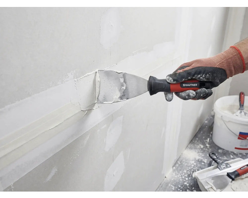 En person spacklar en vägg med spackel och en spackelspade från Rautner.