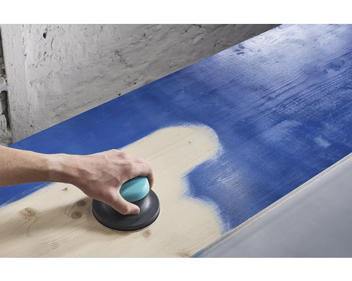 En person slipar en blå träyta med en excenterslipmaskin.