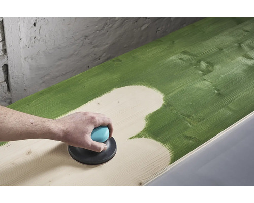 En person slipar en grönmålad träyta med en excenterslipmaskin.