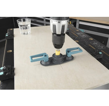 En borrmaskin med kakelborrhjälp borrar i en kakelplatta, ett glas vatten står bredvid.