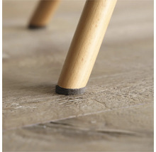 Detaljvy av ett stolsben med filtdyna på trägolv