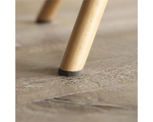 Detaljvy av ett stolsben med filtdyna på trägolv