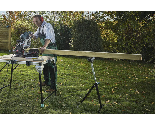 Hantverkare sågar trä med en kap- och gersåg på ett sågbord i trädgården.