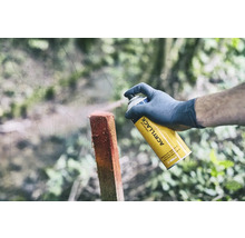 En person sprayar en trästolpe med en gul universal sprayburk