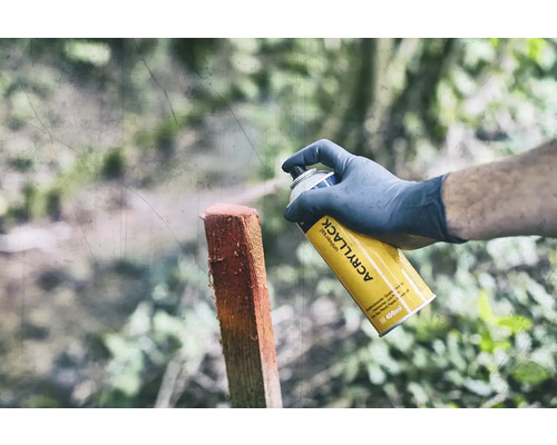 En person sprayar en trästolpe med en gul universal sprayburk