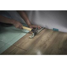 Person lägger laminat med dragjärn och hammare