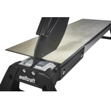 Wolfcraft laminatskärare skär en laminatplanka med trästruktur. Detaljvy av skärmekanismen.