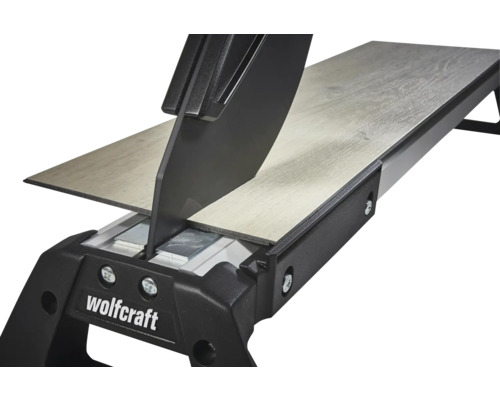 Wolfcraft laminatskärare skär en laminatplanka med trästruktur. Detaljvy av skärmekanismen.