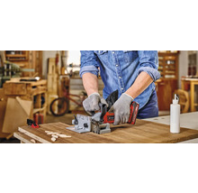 En man använder en notfräs för att bearbeta ett arbetsstycke. Träplattor och en flaska lim ligger på bordet.