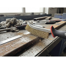 En stålborste rengör en metallbit på en arbetsbänk.