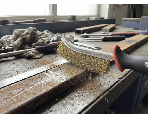 En stålborste rengör en metallbit på en arbetsbänk.