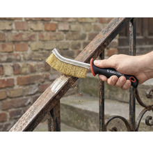 En hand använder en stålborste för metallrengöring på ett räcke. Rautner logotyp synlig.