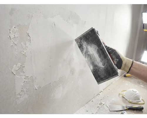 Hantverkare slipar vägg med slipverktyg. Gör-det-själv-projekt för väggrenovering.