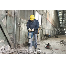 Man med skyddshjälm och hörselskydd använder en bilningshammare inomhus.