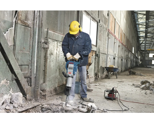 Man med skyddshjälm och hörselskydd använder en bilningshammare inomhus.