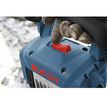 Hand med handske manövrerar den röda strömbrytaren på en blå Bosch bilningshammare.