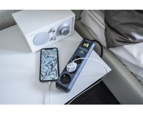 Grenuttag med överspänningsskydd och ansluten telefon på ett nattduksbord