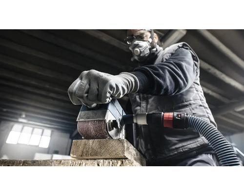 En man slipar en träbit med en slipmaskin. Han bär ett skyddsmask och skyddsglasögon.