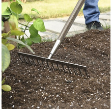 Trädgårdsräfsa med träskaft som används på trädgårdsjord.