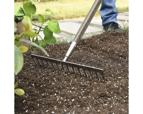 Trädgårdsräfsa med träskaft som används på trädgårdsjord.