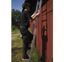 En person klättrar på en aluminiumstege mot en röd trävägg.