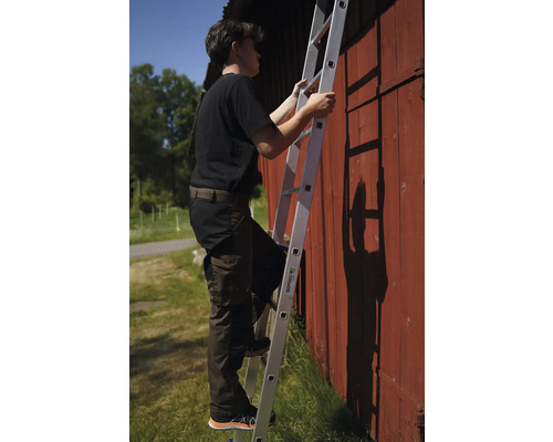 En person klättrar på en aluminiumstege mot en röd trävägg.