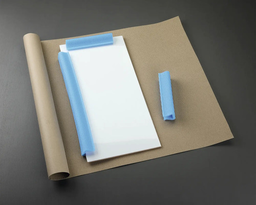 Förpackningsmaterial: glasplatta, pappersrulle, wellpapp och skumskydd.