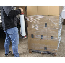 En person packar kartonger med en folieomslagare på en pall.