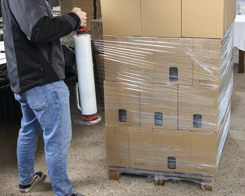 En person packar kartonger med en folieomslagare på en pall.