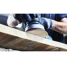 En person slipar en träplanka med en excenterslipmaskin.