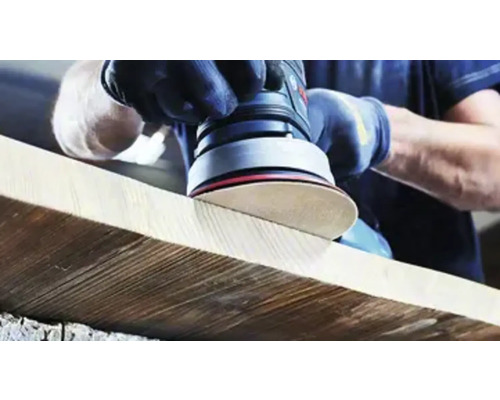 En person slipar en träplanka med en excenterslipmaskin.