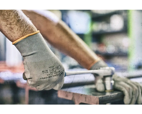 En person bär skyddshandskar och använder en skiftnyckel.