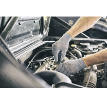 En mekaniker som arbetar med skyddshandskar på en bilmotor.